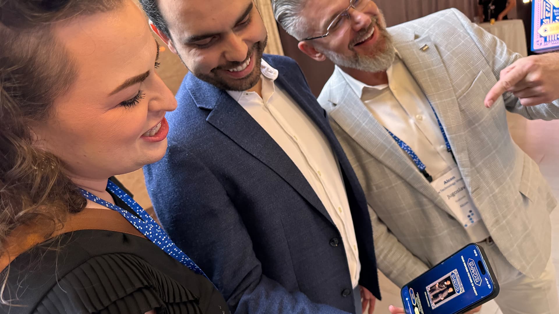 Event photograph, Alcon reception, June 2026; published June 11. Guests view the themed video page on a phone. The original framing and background are preserved.